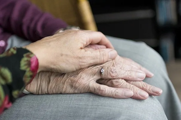 Eine Hand liegt unterstützend auf der Hand einer älteren Person